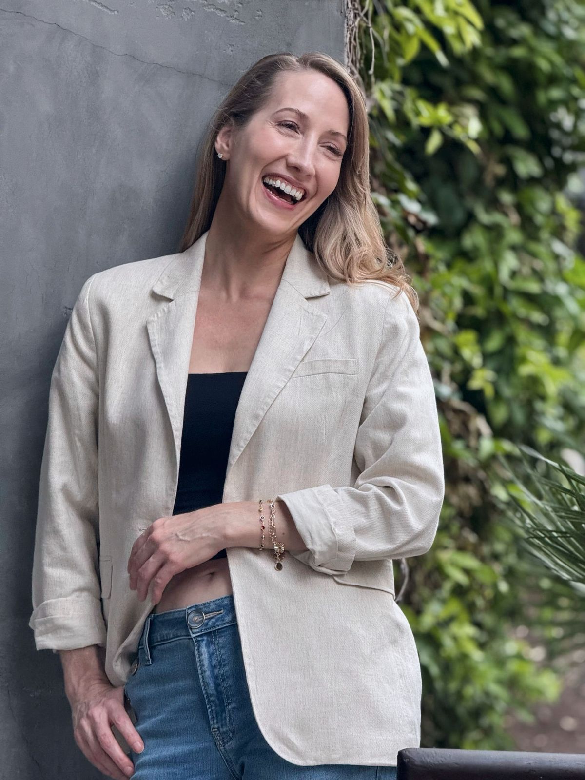 Erin Warner laughing, wearing a linen blazer beside greenery