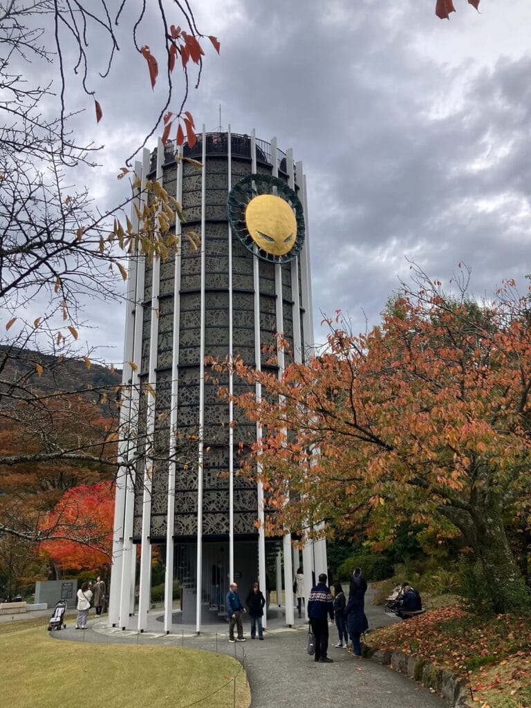 The Symphonic Sculpture tower at Hakone Open Air Museum with a large golden circle on its facade, surrounded by autumn trees
