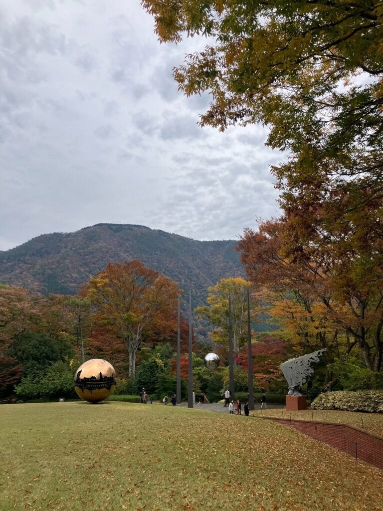 Reflective sphere sculptures on the lawn at Hakone Open Air Museum with autumn mountains in the background