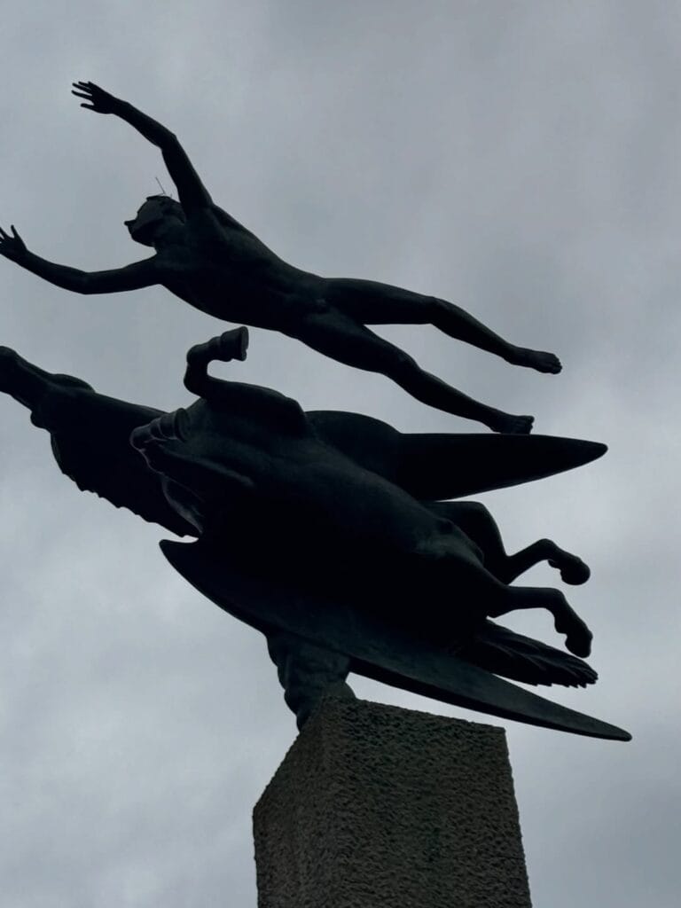 Bronze sculpture of two figures in dynamic flight silhouetted against a grey sky at Hakone Open Air Museum