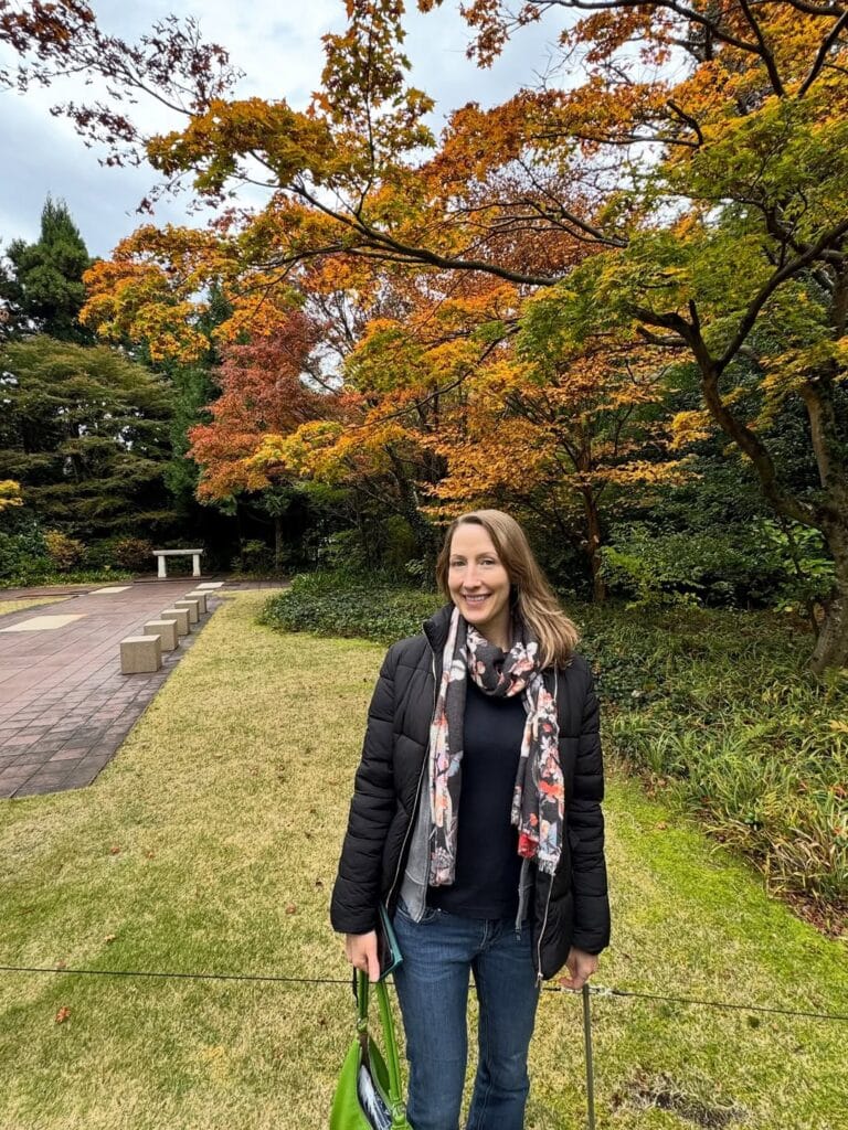 Erin Warner smiling in front of vivid orange and yellow autumn foliage at Hakone Open Air Museum