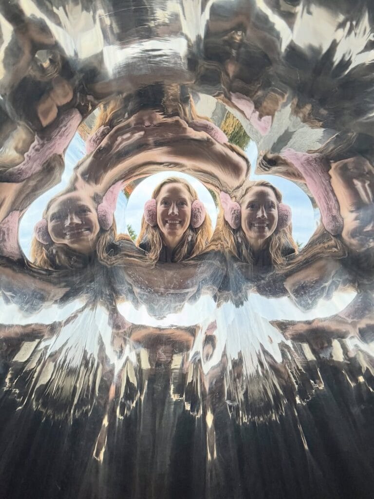 Erin Warners reflection multiplied inside a curved mirrored sculpture at Hakone Open Air Museum