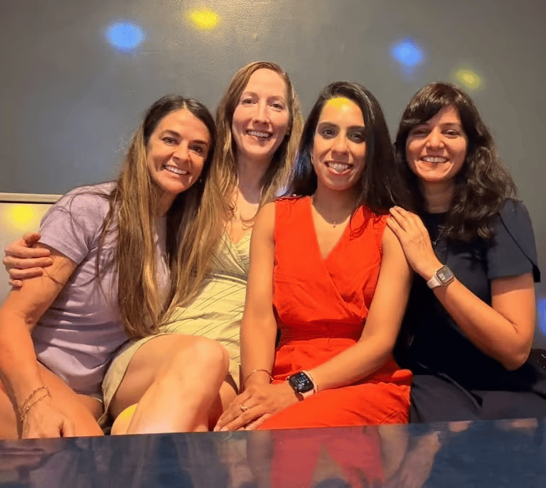 Four women smiling together on a bench in a private karaoke room